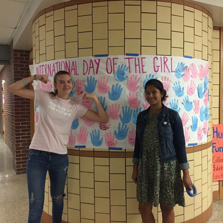 Kailey Gielink (left) and Praditha Behara (right) hanging up a poster for International Day of the Girl.